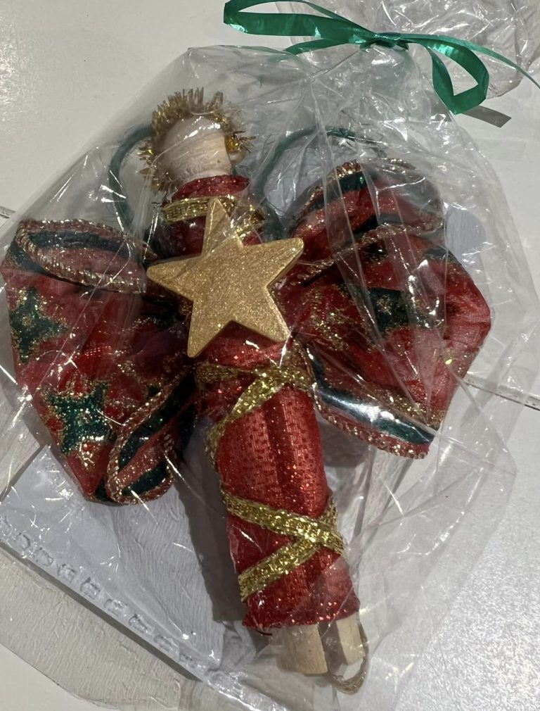 A wooden clothes pin that has been wrapped in red plaid ribbon to look like an angel.