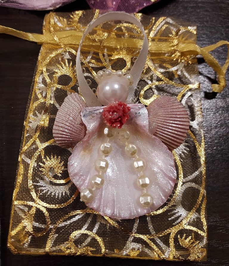 An ornament made of various seashells and beads glued together to look like an angel.