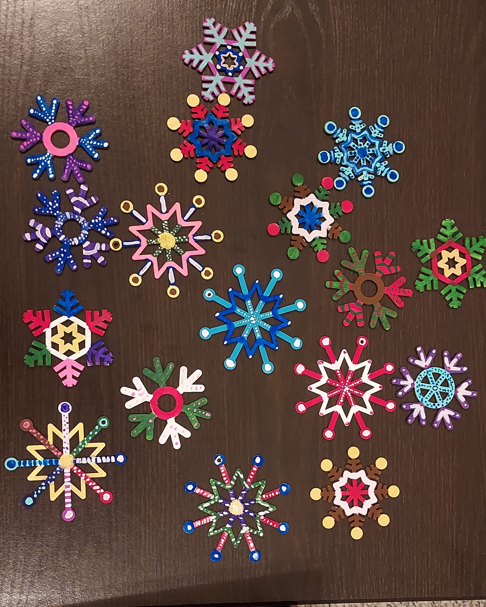 A variety of colorful snowflake ornaments made from painted popsicle sticks.