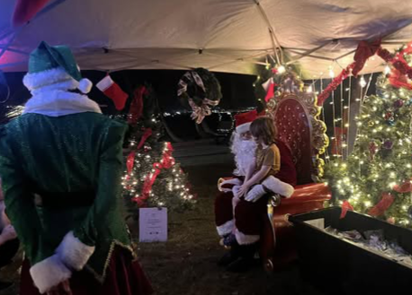 Santa handing out ornaments under an outdoor tent.