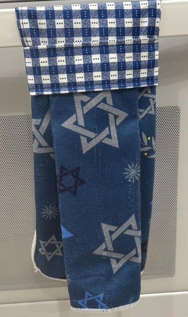 A dark blue kitchen towel with silver stars of David and a blue and white checked border on top.
